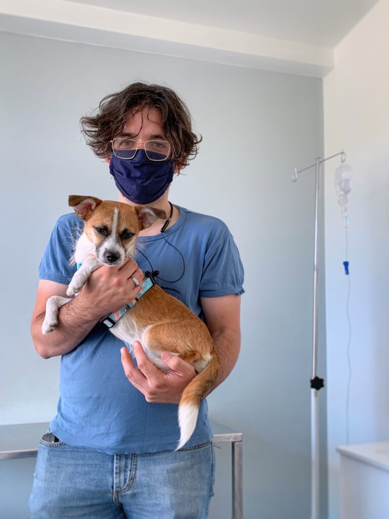 Zdjęcie mężczyzny w maseczce w lecznicy weterynaryjnej trzymającego na rękach małego psa